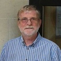 Alan has glasses, grey hair and a short beard.